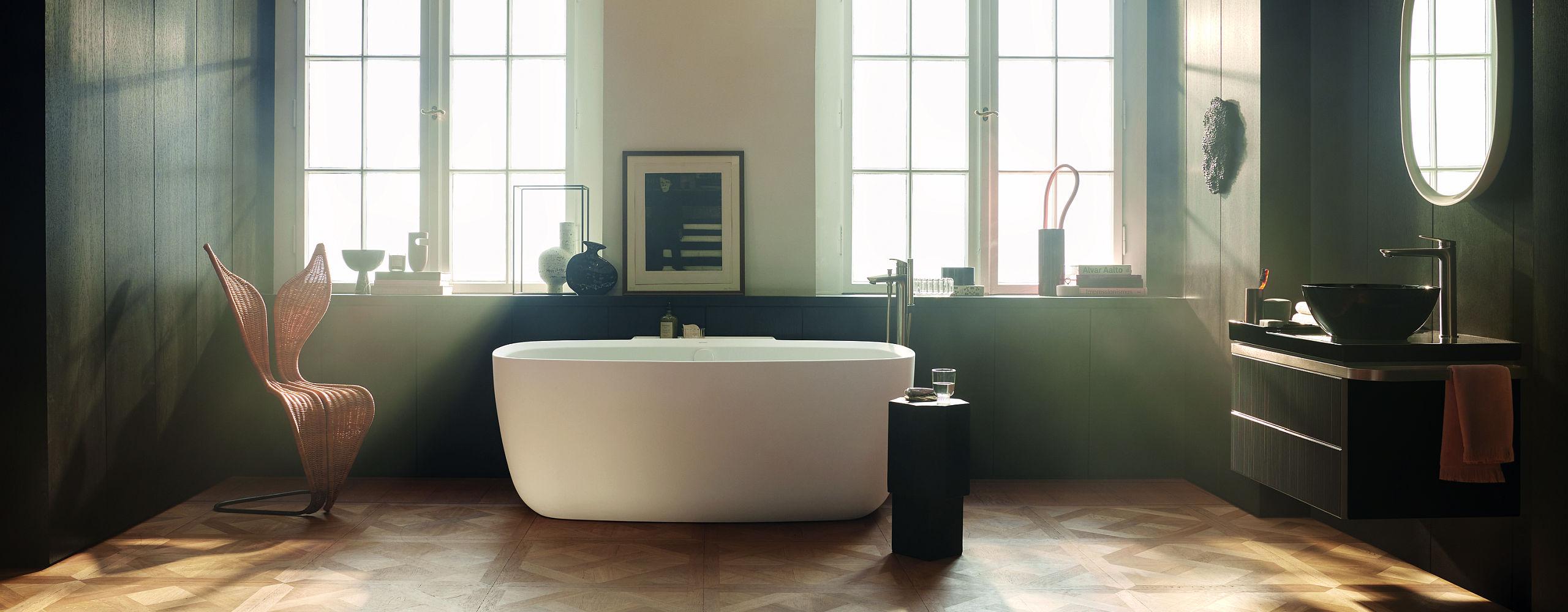 Elegantes Badezimmer mit freistehender Badewanne, großen Fenstern und stilvollen Accessoires wie Vasen und Büchern.