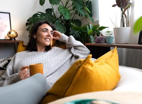 Enntspannte Frau auf Couch mit Teetasse.