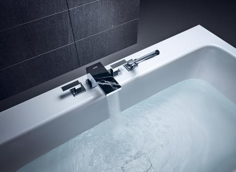 Eine moderne Badewanne mit einer stilvollen, rechteckigen Armatur aus glänzendem Metall und einer schwarzen Marmoroberfläche.