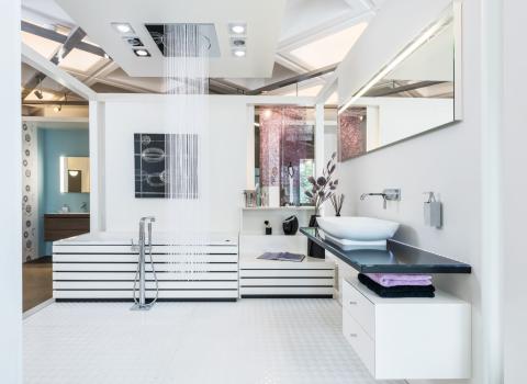 Ein luxuriöser Showroom von Mundle in Sindelfingen mit einer modernen Badewanne, einer Regendusche von der Decke und einem stilvollen Waschbereich.