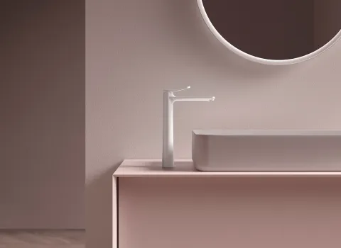 Eine hohe, schlanke Waschtischarmatur der Serie Frattini FLÒ steht auf einem zartrosa Badmöbel und harmoniert mit dem modernen Waschbecken und dem runden Spiegel darüber.