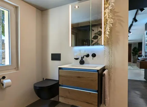 Modernes Gäste-WC mit schwebendem Waschtisch in Holzoptik, beleuchtetem Spiegelschrank und schwarzem Wand-WC.