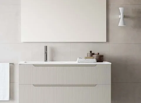 Stocco Badmöbel mit geriffelter Front in Elfenbein und großem Spiegel vor Fliesenwand.