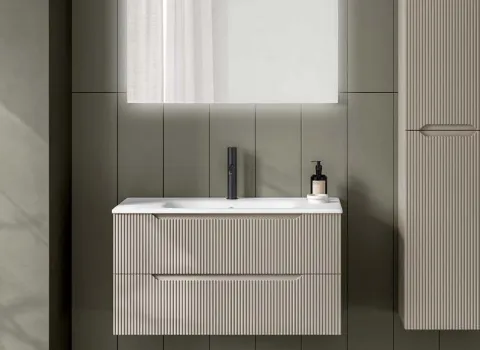 Badmöbel mit geriffelter Front in Elfenbein und passendem Hochschrank vor grüner Wand.