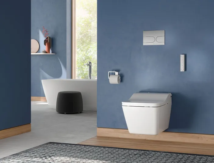 Großes Badezimmer mit blauen Wänden, einem wandhängenden TOTO-SW-WC und einer freistehenden Badewanne im Hintergrund.