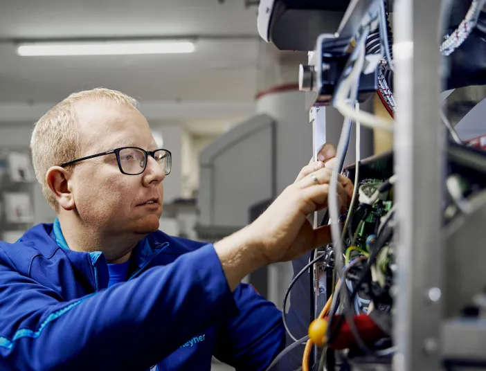 Ein Elektriker arbeitet an einer Elektroinstallation, indem er Drähte und Schaltkreise in einem Gerät überprüft.