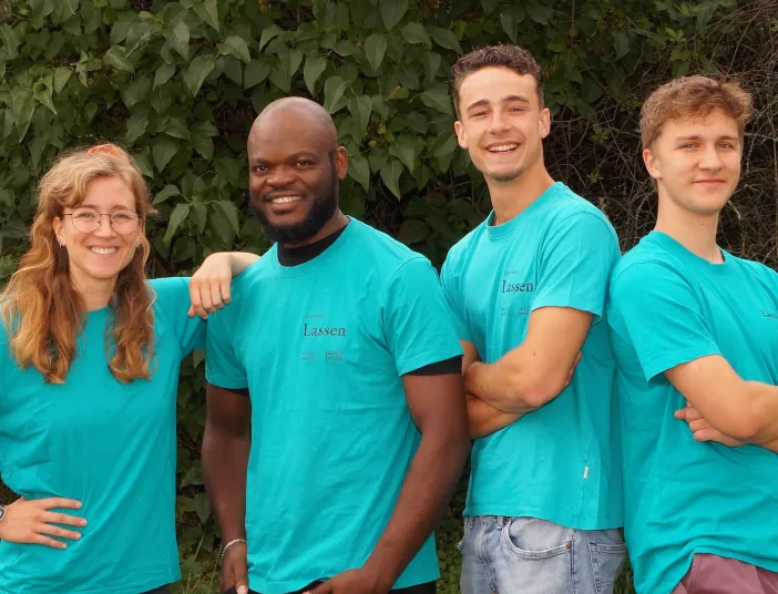 Eine Gruppe von vier jungen Azubis in türkisfarbenen Team-Shirts posiert lächelnd vor einer Hecke.