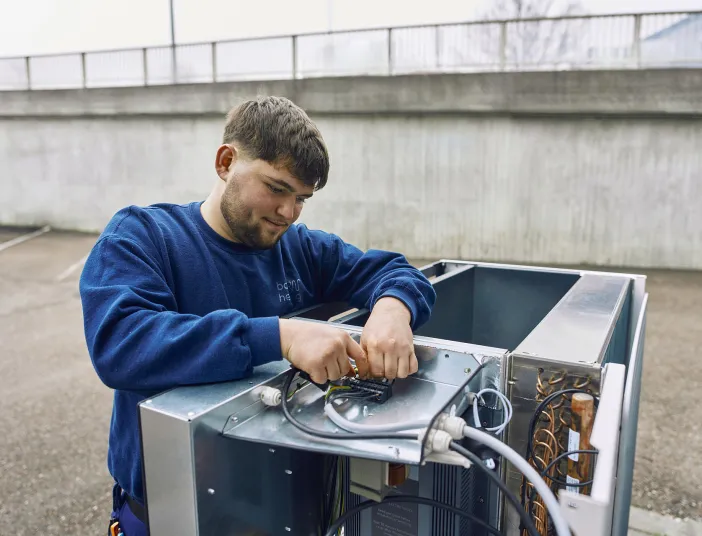 Ein junger Elektriker in blauer Arbeitskleidung repariert eine industrielle Elektroanlage im Freien.