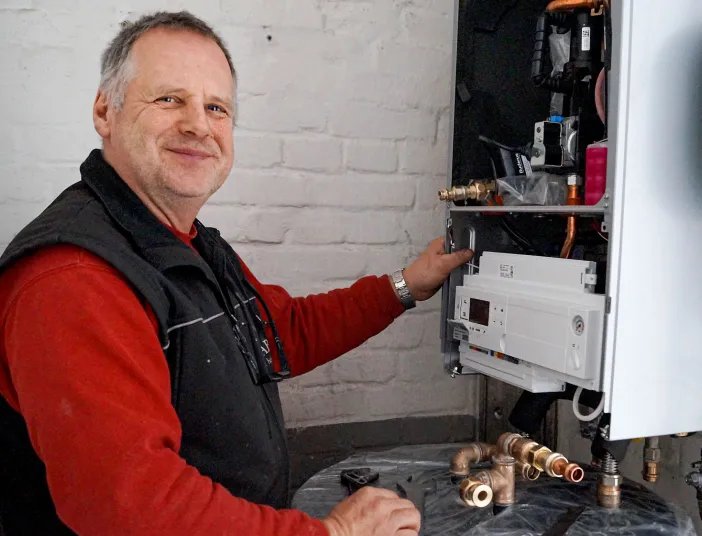 Ein Heizungsmonteur der Firma Laabs wartet eine Gastherme, umgeben von Kupferrohren und Werkzeugen. 