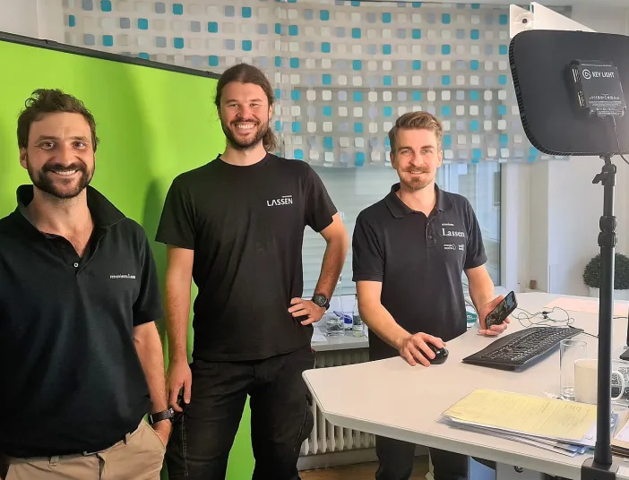Drei Energie-Experten der Firma Lassen aus Freiburg stehen im Bürozimmer und lächeln in die Kamera.