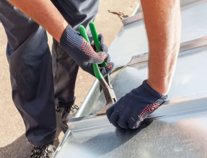 Ein Klempner bearbeitet mit einer Zange eine Metallabdeckung am Dach.