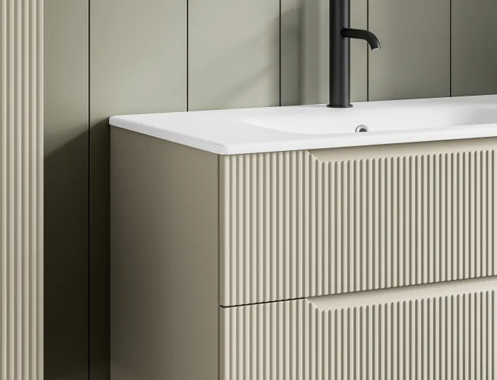 Detailansicht eines wandhängenden Waschtischs mit geriffelter Front in Elfenbein und schwarzer Armatur.